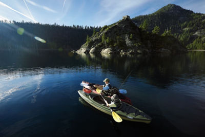 Two people fly fishing in kayaks in a lake surrounded by trees