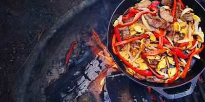 A pan cooking fajitas over a campfire