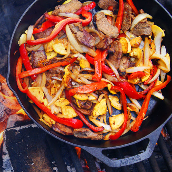A pan cooking fajitas over a campfire