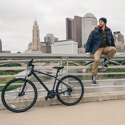 Cyclist sitting on bridge in front of Columbus Skyline with bike next to him