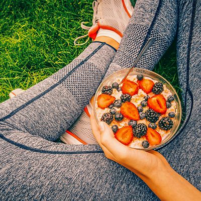 A woman sitting on the grass eating oatmeal with berries after a run
