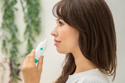 Young woman holding up a Fluo Labs nasal device to her nose at home. 