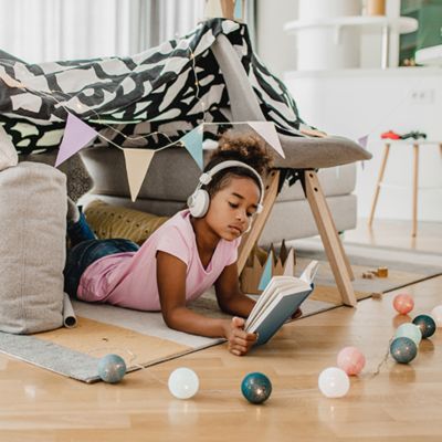 Child reading a book under home made tent. 