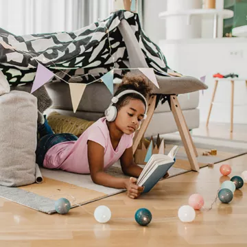 Child reading a book under home made tent. 
