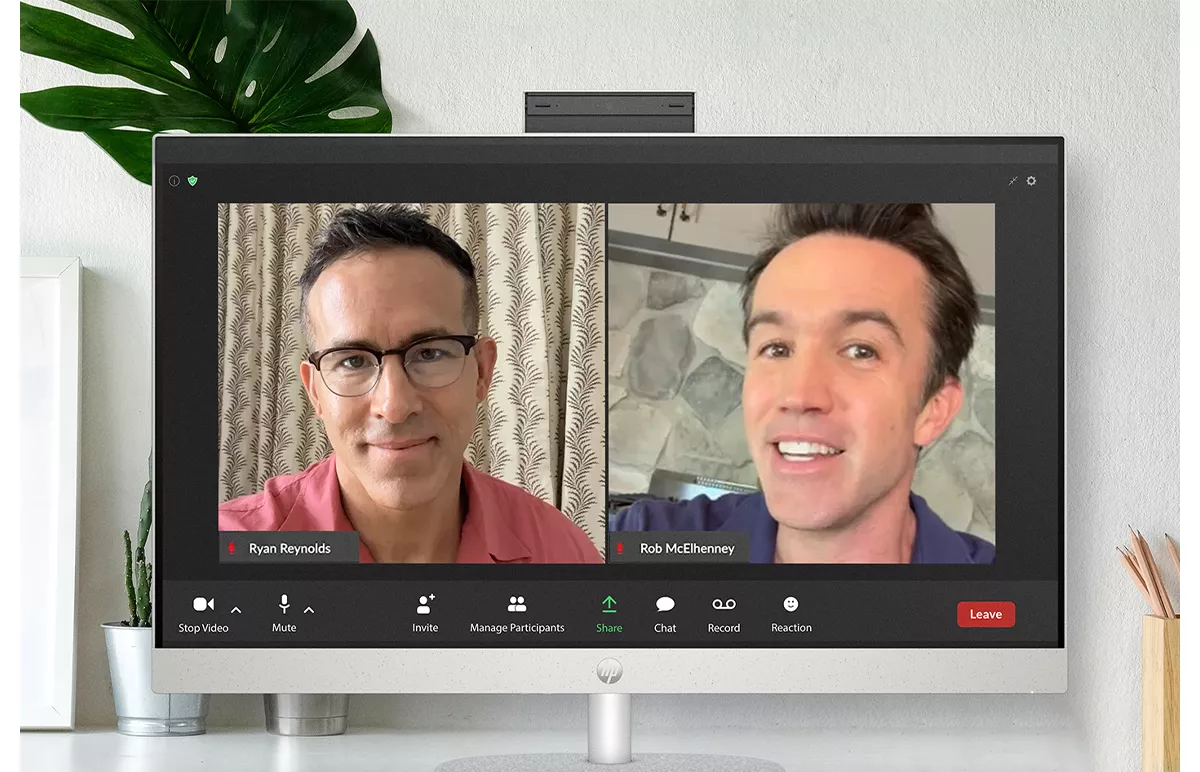 Ryan Reynolds and Rob McElhenney smiling on a split-screen Zoom call on an animated HP desktop computer .
