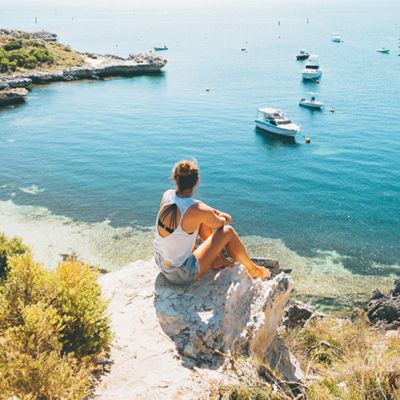 Traveling woman sitting on rock looking at longreach bay on Rottnest Island near Perth, Australia. 
