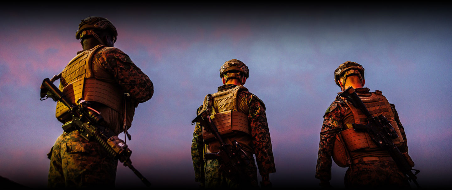 Three Marines in full tactical gear with rifles standing against twilight sky during field operation.