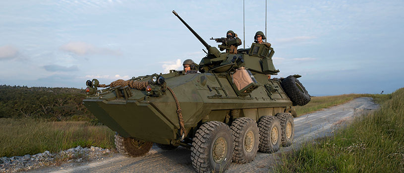 Marines operate LAV-25 light armored vehicle with turret-mounted cannon on coastal road during training in Japan.
