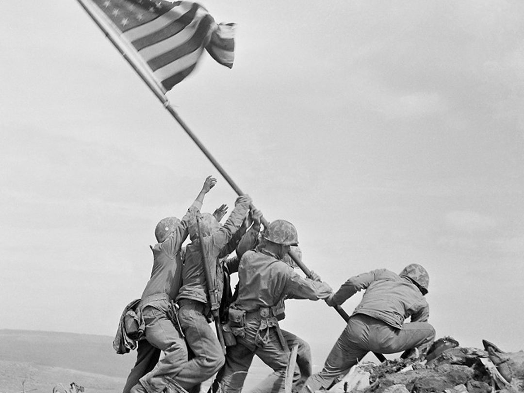 Historic black and white photo of Marines raising American flag on Mount Suribachi at Iwo Jima.