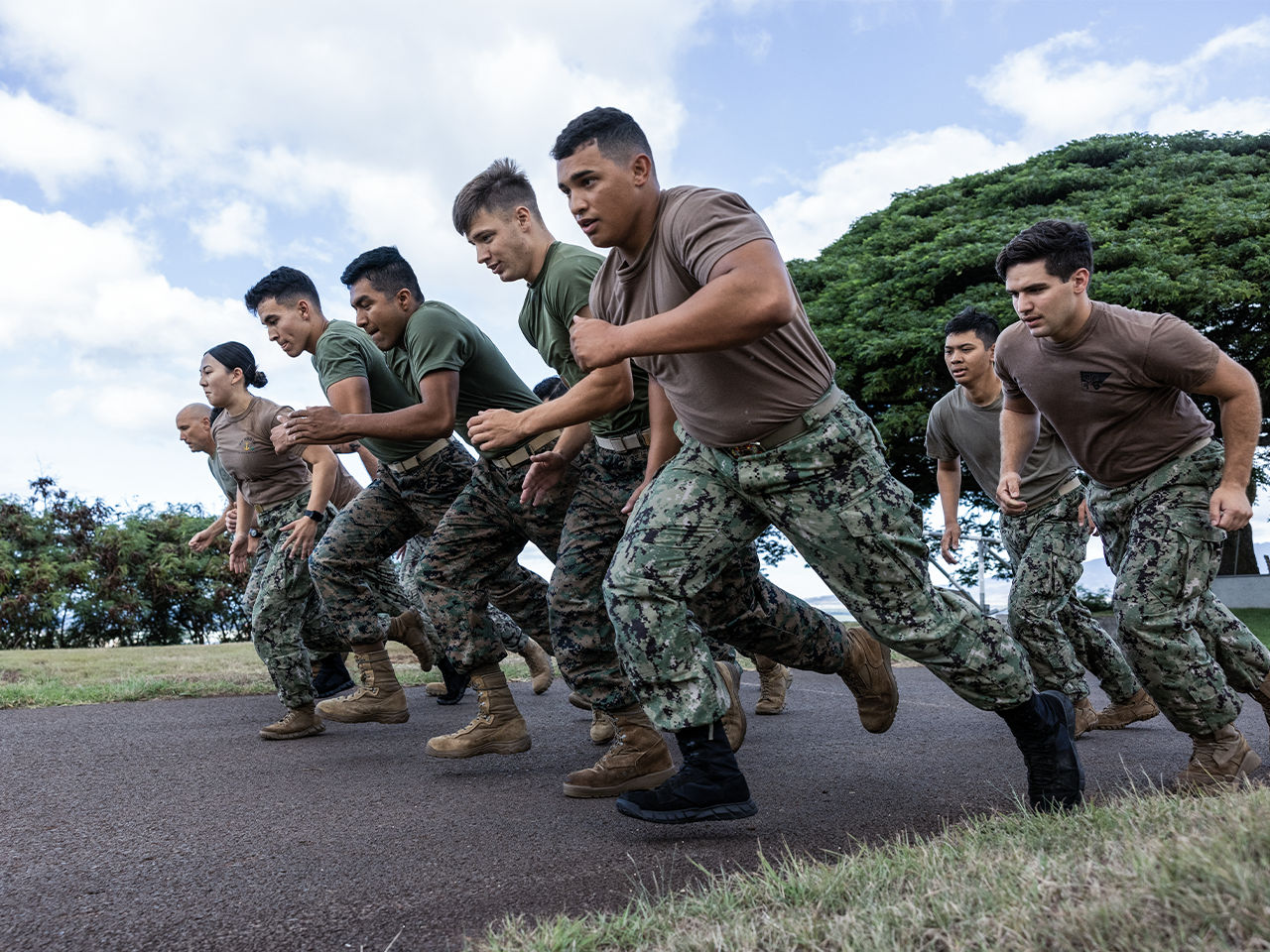 Group of Marines in camouflage uniforms running in formation during physical training outdoors.