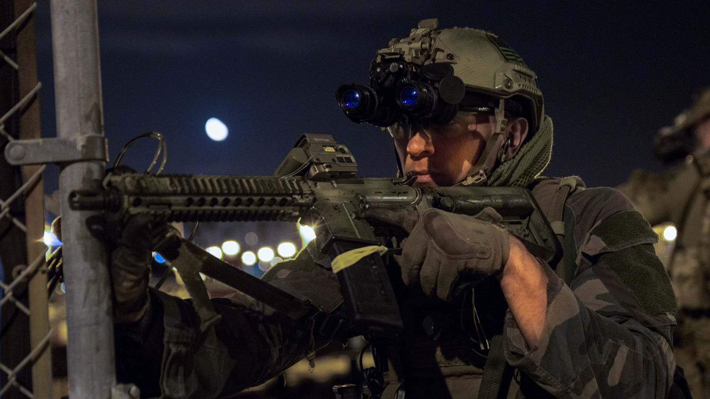 Marine aiming rifle with night vision goggles during nighttime tactical operation.