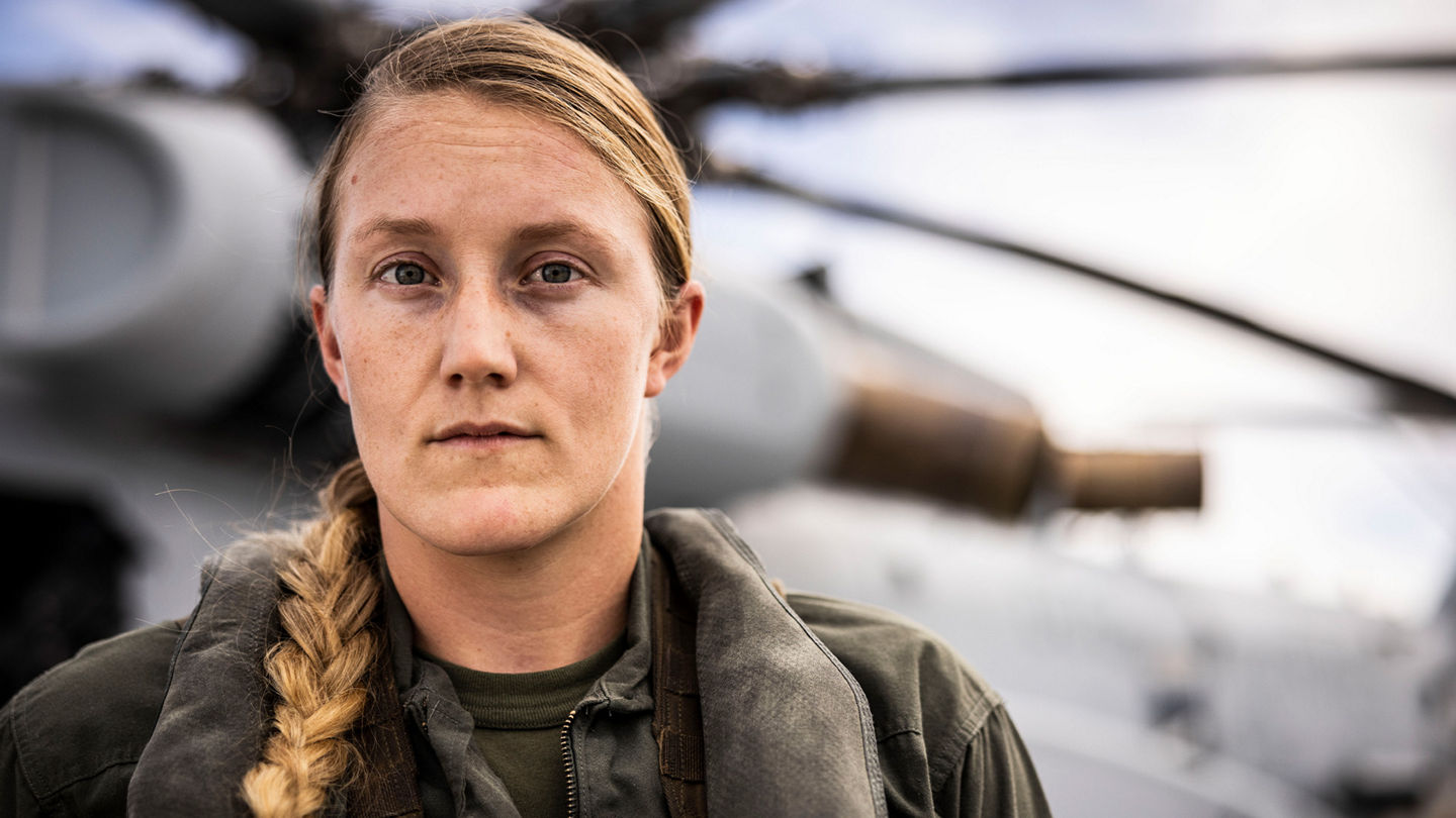 Captain Kricket Harper in flight suit stands on flight line with helicopter in background at Camp Lejeune.