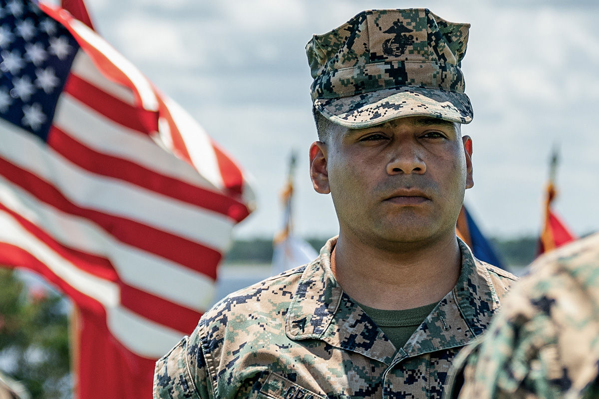 Lance Corporal Kevin Grajeda stands at attention with American flag in foreground during outdoor military ceremony.