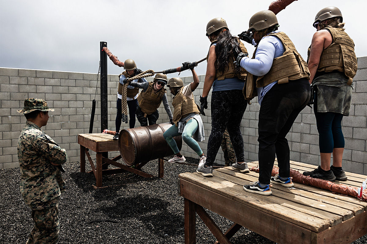 Officer candidate observes team navigate rope obstacle course during leadership training exercise wearing protective gear.
