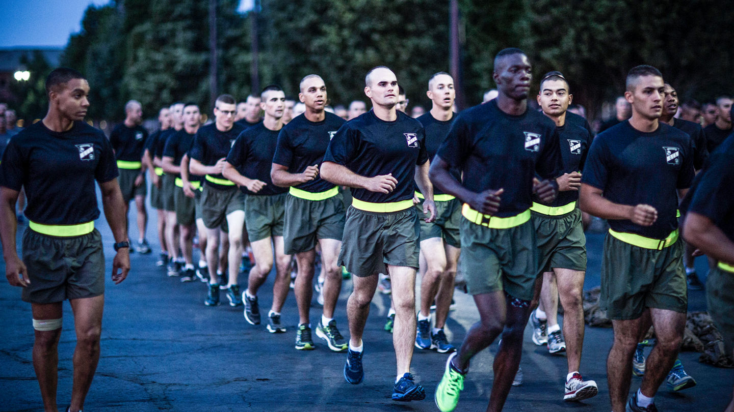 Marine officer candidates running in formation wearing black shirts and green shorts with yellow belts.
