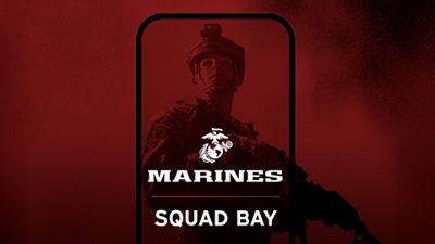 A Marine in tactical gear with a rifle, framed by a phone outline, on a red background. USMC logo, "MARINES SQUAD BAY" text.