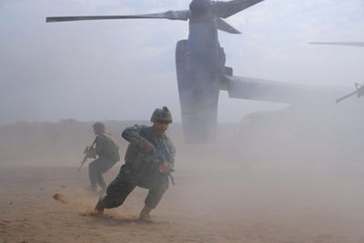 Marines exit V-22 Osprey aircraft during amphibious assault training operation in dusty desert conditions.