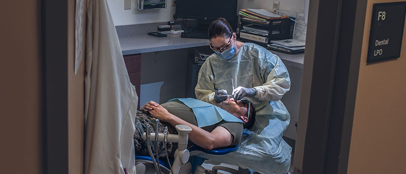 Military dental professional providing dental treatment to Marines patient in clinical setting.