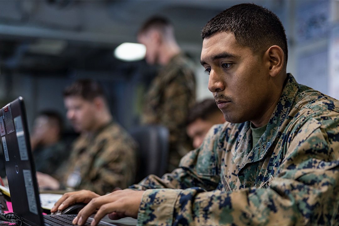 An Administrative and Data Specialist Marine works at a computer in a command center alongside other Marines. 