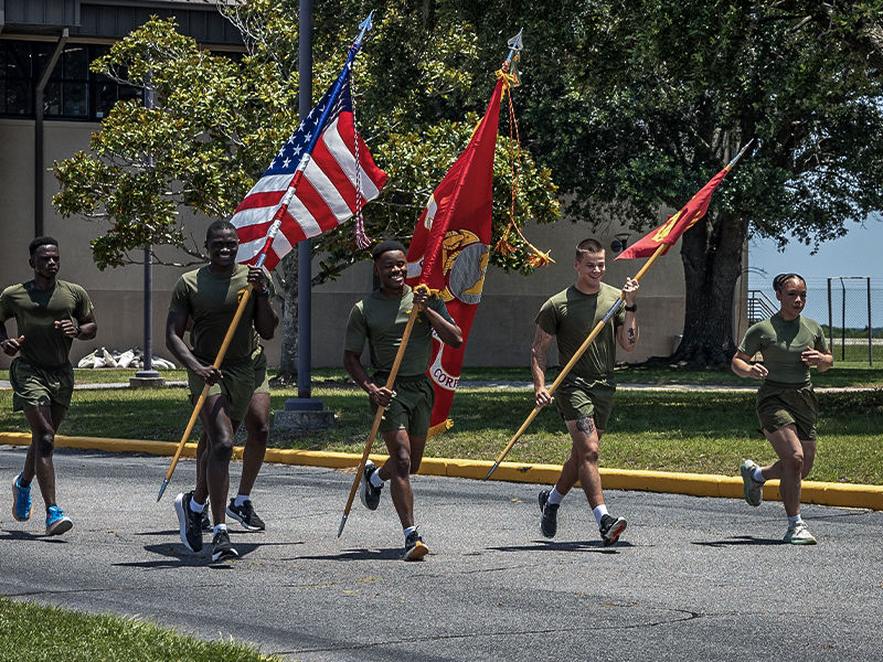Marines conducting physical training holding the United States of America and the Marine Corps flags. 
