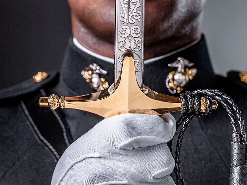 A Marine in dress blues holding a Mameluke sword.
