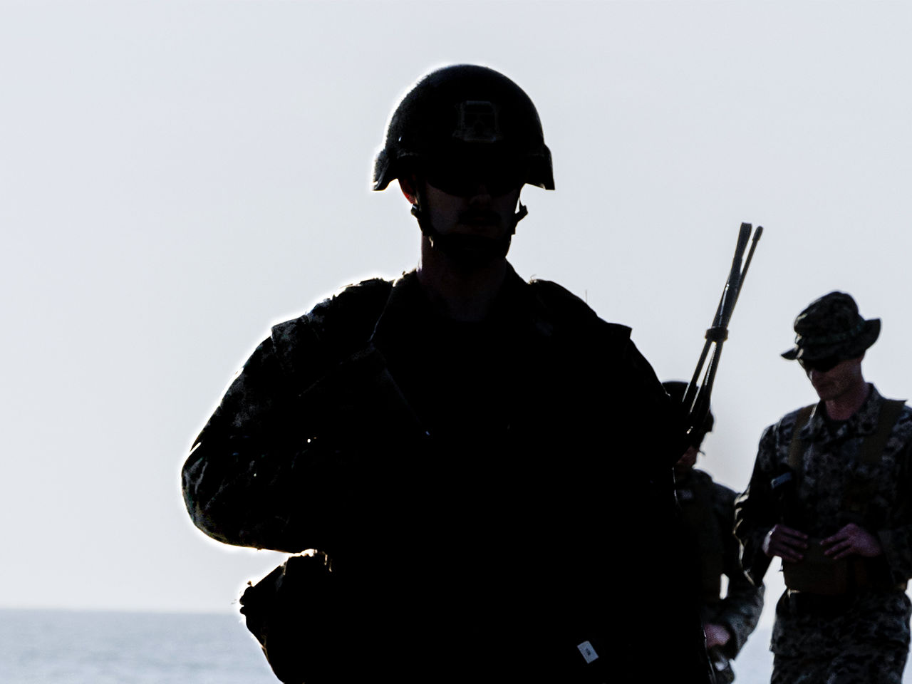  Silhouette of Marine with rifle standing security watch against bright sky background.