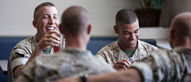 Marines sharing meal and conversation together in dining facility, demonstrating camaraderie during mealtime.