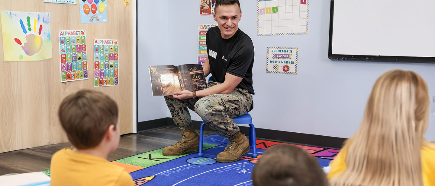 Marine reading to children in classroom, demonstrating community engagement and family life activities.