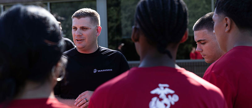 Marine recruiter in black shirt providing guidance and coaching to poolees in Delayed Entry Program.