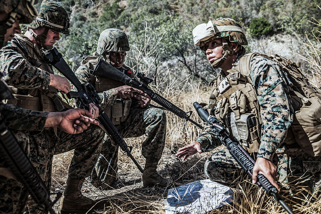 Marines in camouflage uniforms with rifles conducting tactical field training exercise in natural terrain.