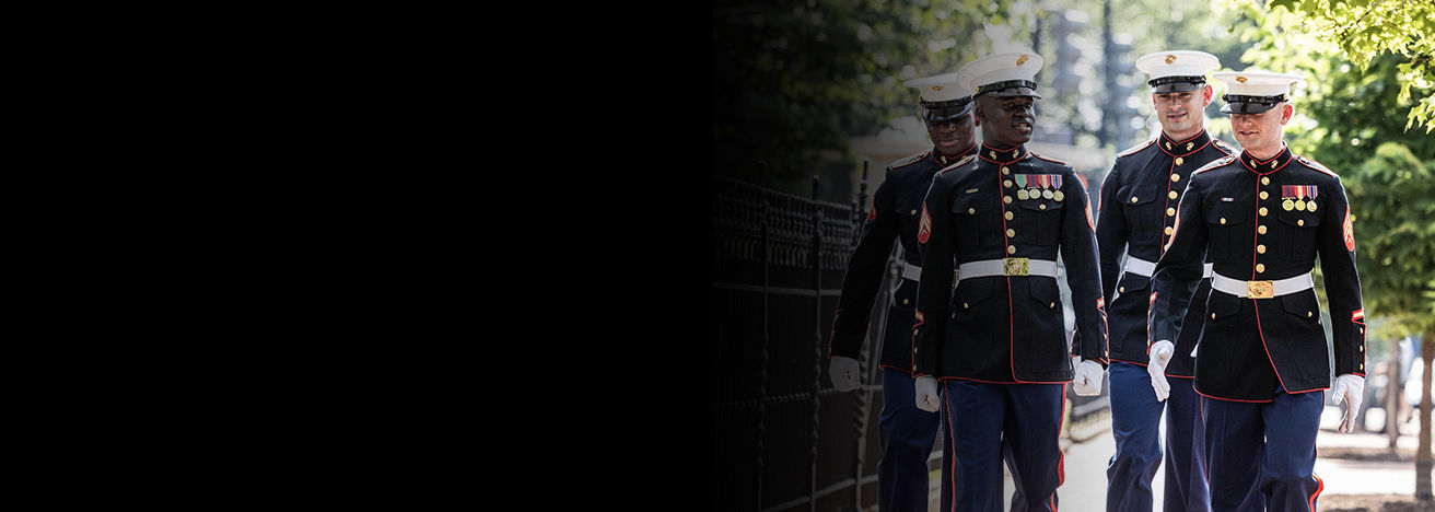 Marines in dress blue uniforms walking in formation at Marine Barracks Washington during ceremonial duty.