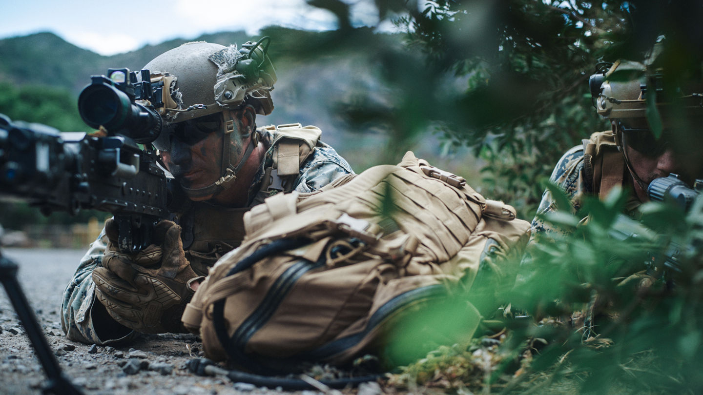 Marines in prone position using advanced optics and equipment during tactical field training exercise.