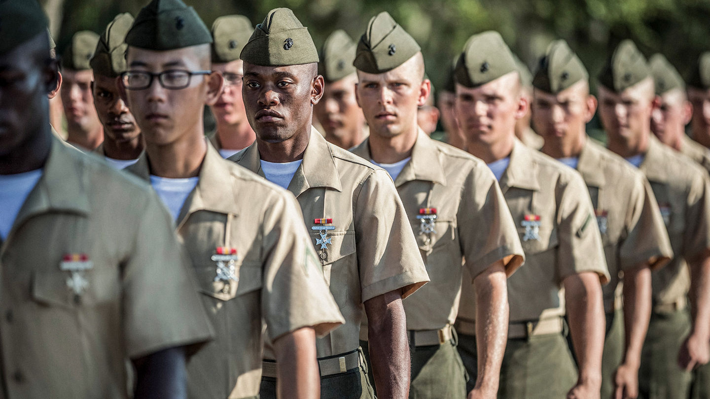 Marines in tan service uniforms with garrison caps and ribbons standing in formation displaying military distinction.