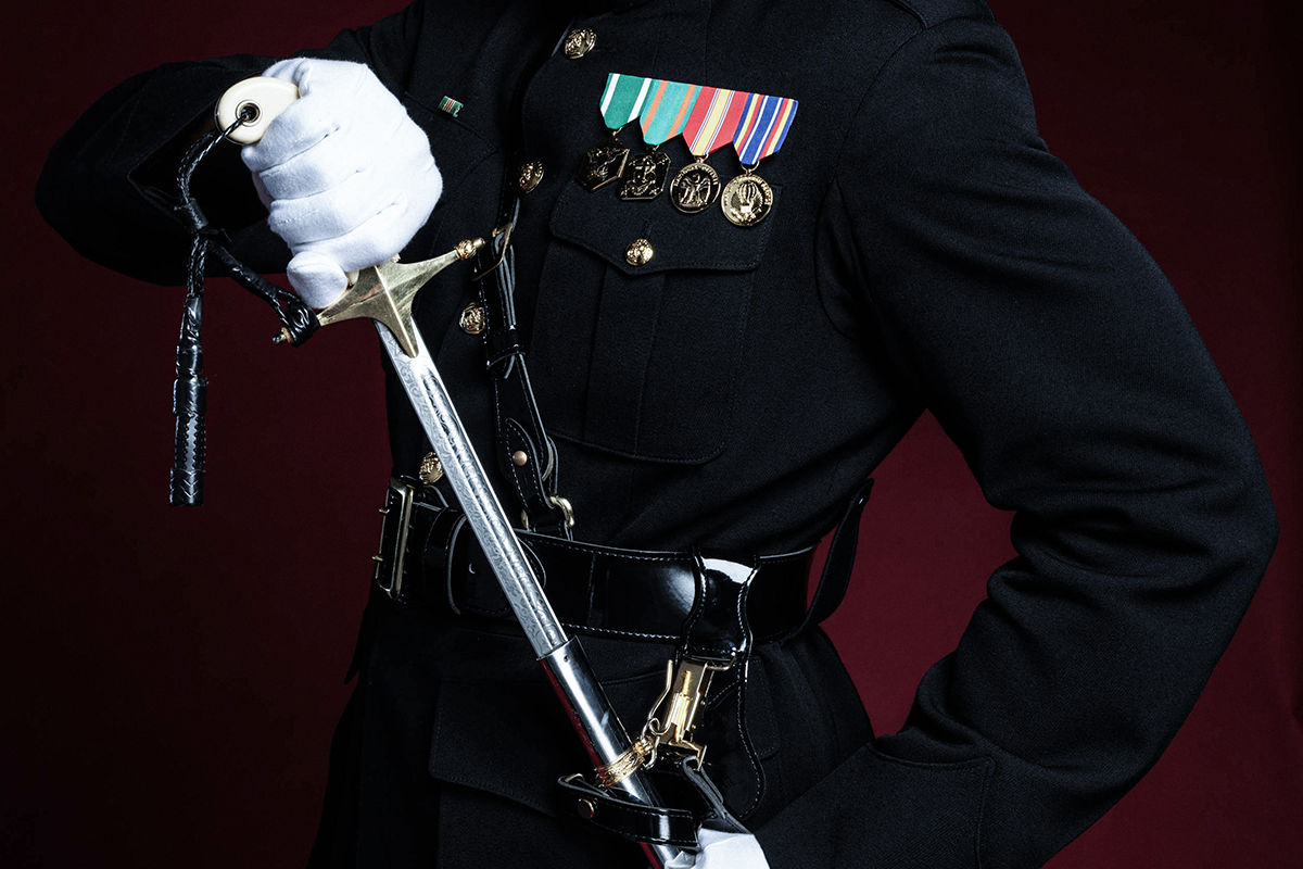 Marine in dress blue uniform with ribbons and medals holding ceremonial Mameluke sword with white gloves.