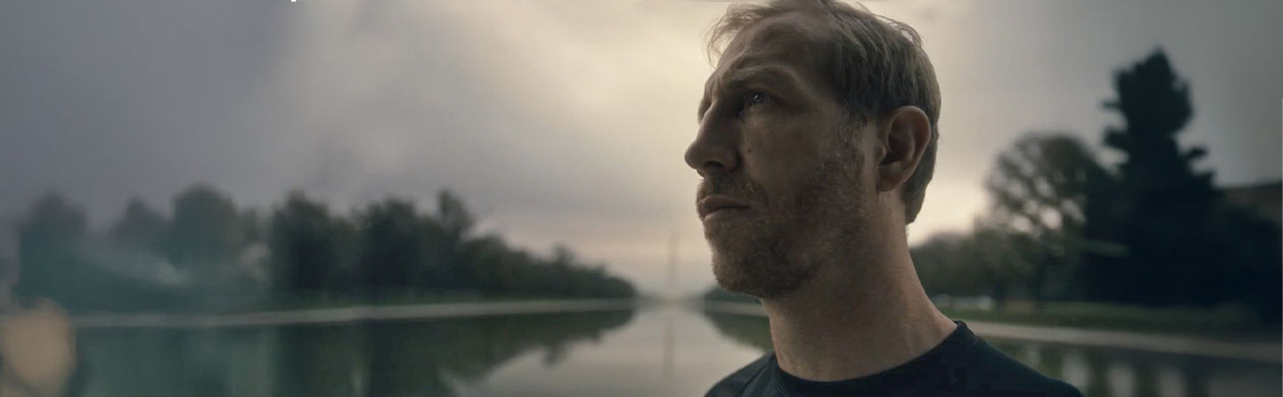 Marine veteran Jake Harriman looks upward outdoors with water and trees in background.
