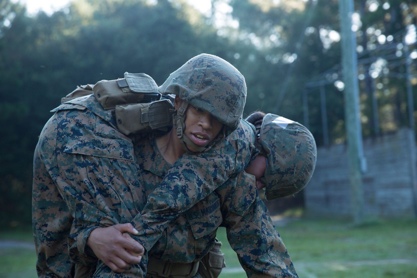 A Marine Corps recruit carries a fellow recruit across his shoulders in a fireman's carry during a training exercise at dusk.