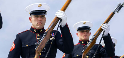U.S. Marines in dress blues stand in formation with their rifles. 