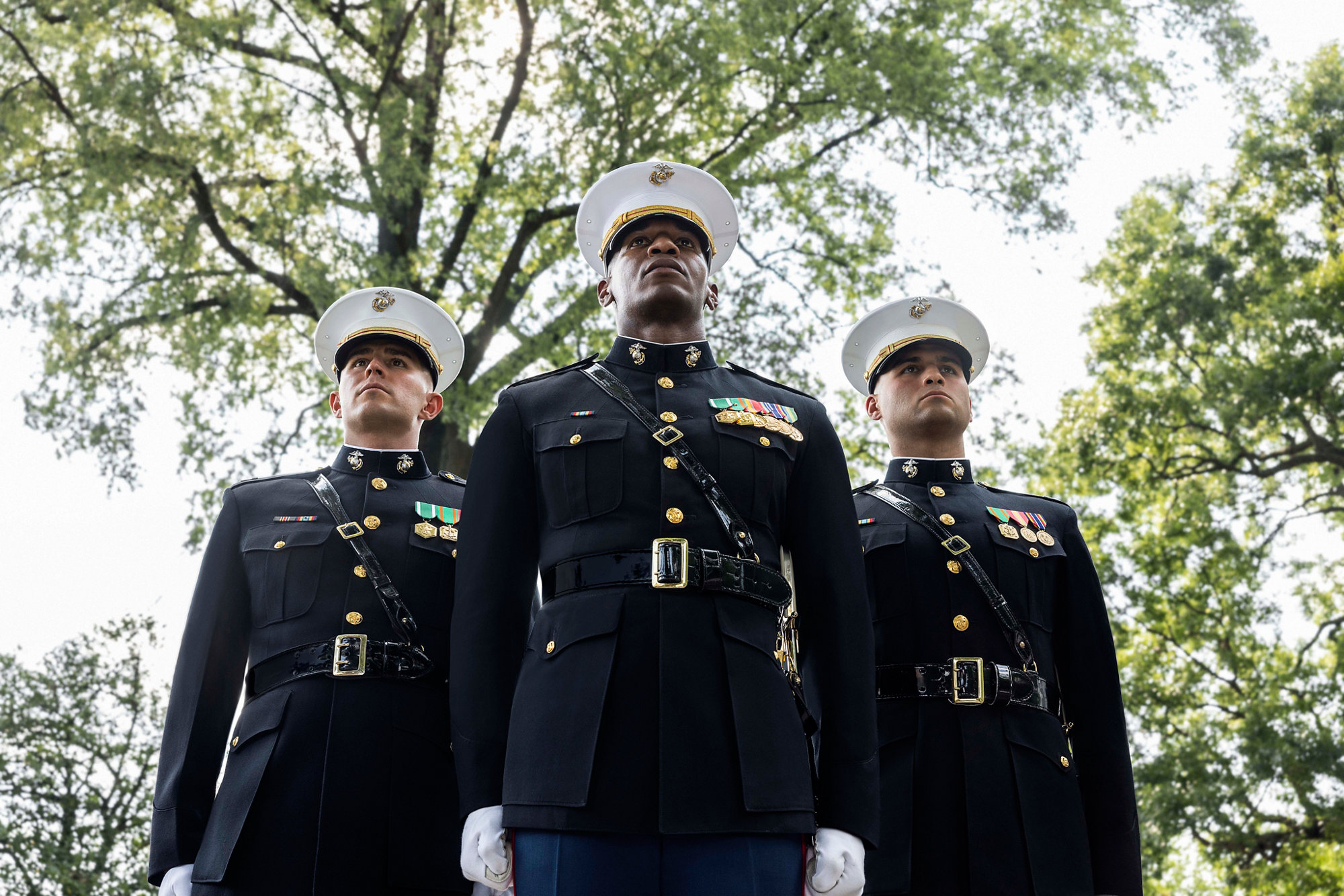Three Marine officers in dress blue uniforms with service ribbons standing outdoors in formation.