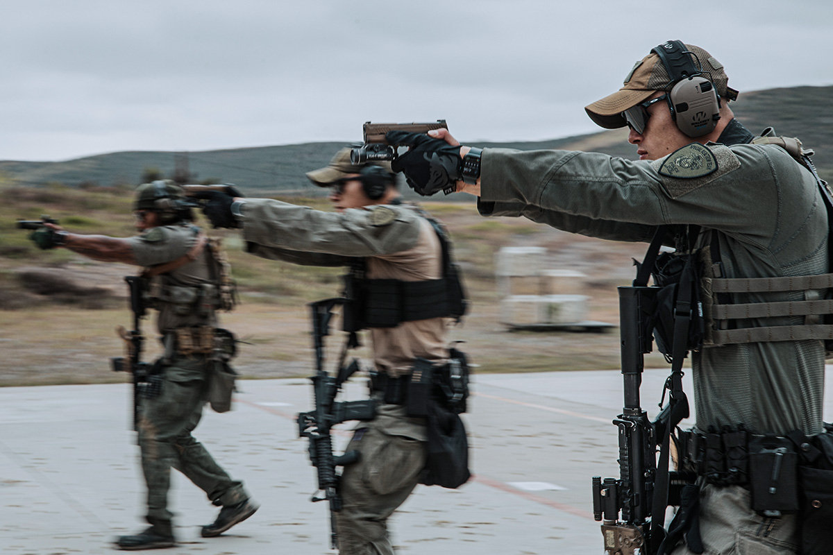 Three law enforcement Marines train with their firearms on the range. They have pistols drawn and carry rifles. 