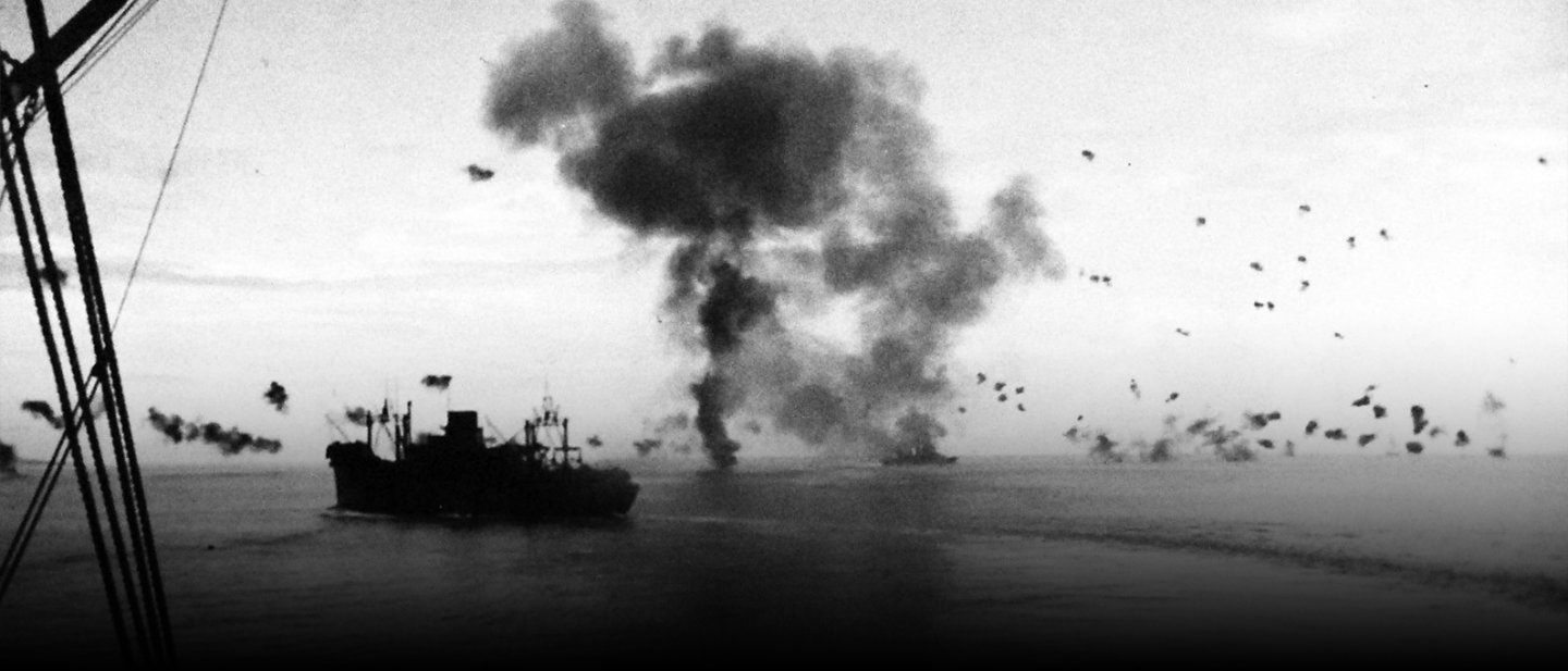 Historical photo of landing craft approaching Guadalcanal beach with explosions during amphibious assault in 1942.