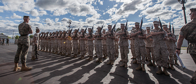 Officer candidates stand in formation holding rifles during Phase 2 drill inspection under blue sky with clouds.
