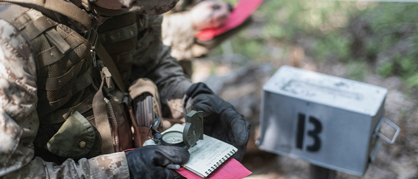 Officer candidate uses compass and map to navigate during Phase 3 land navigation training exercise.