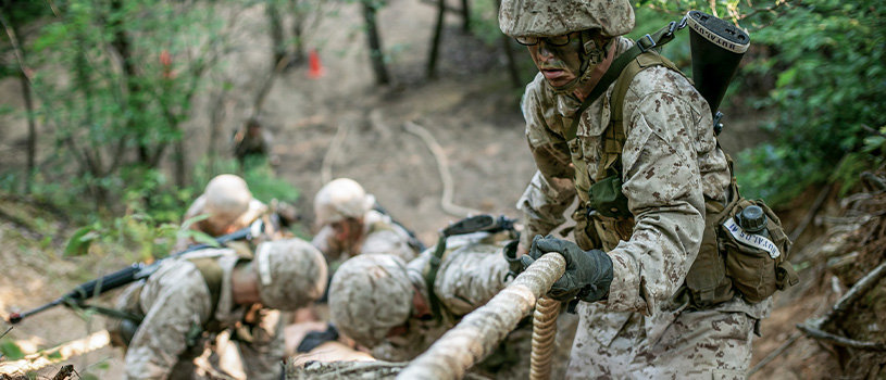 Officer candidate rappels down slope while others practice rope techniques during Phase 4 field training exercise.