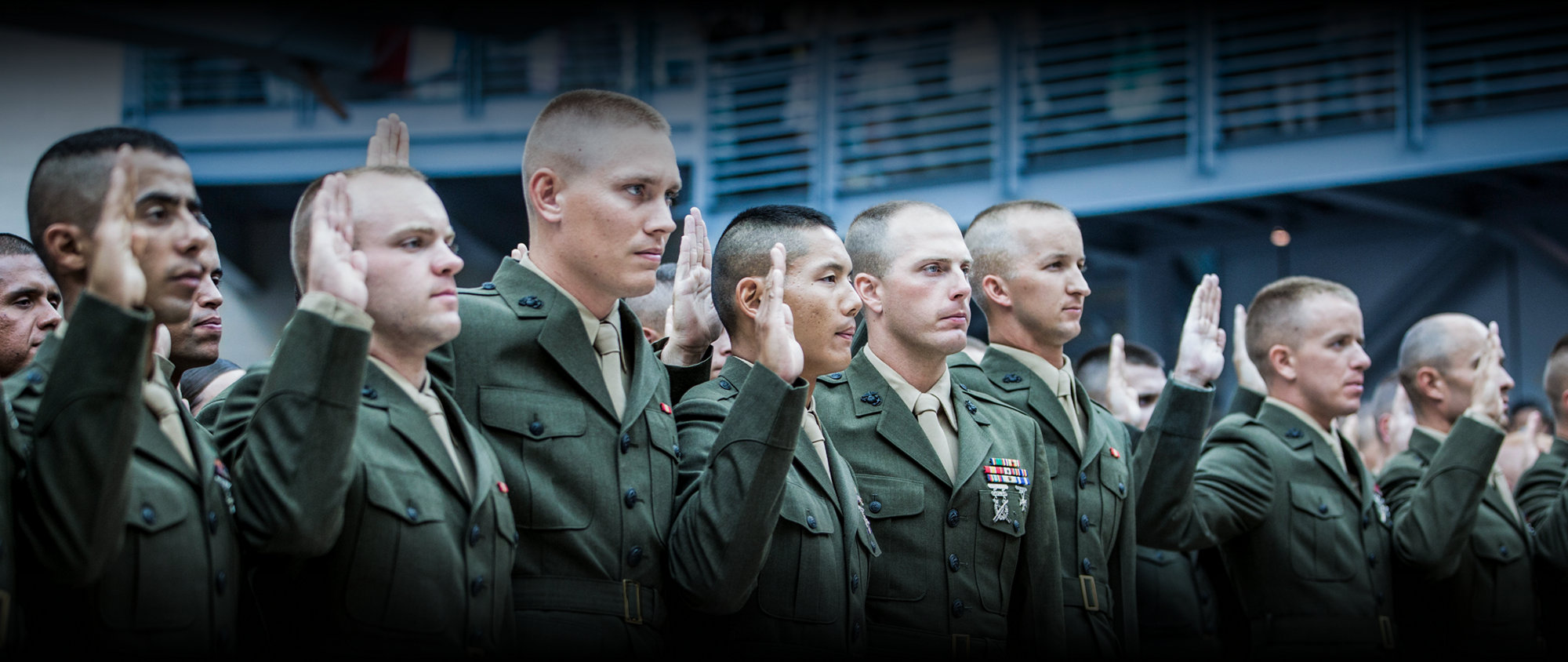 Marines in service green uniforms taking oath with raised hands during formal commissioning ceremony.