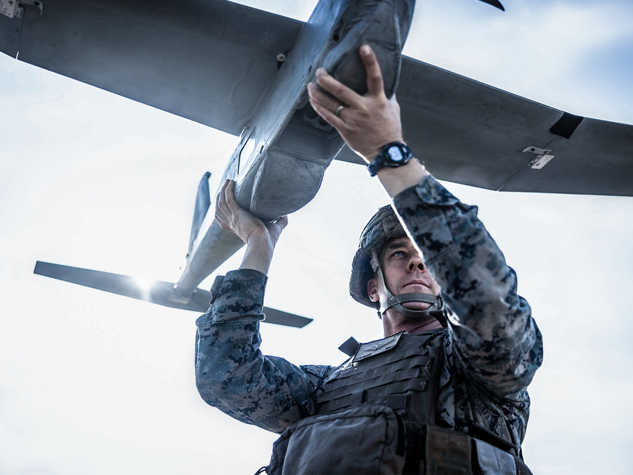 Marine in camouflage and tactical vest inspecting military aircraft wing during maintenance operations.