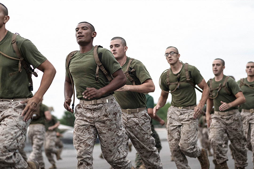 Group of Marine recruits in desert camouflage running in formation during Physical Fitness Test training.