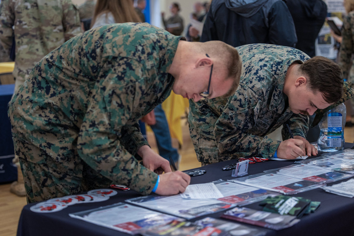 Two Marines in digital camouflage reviewing educational materials and brochures at information booth.