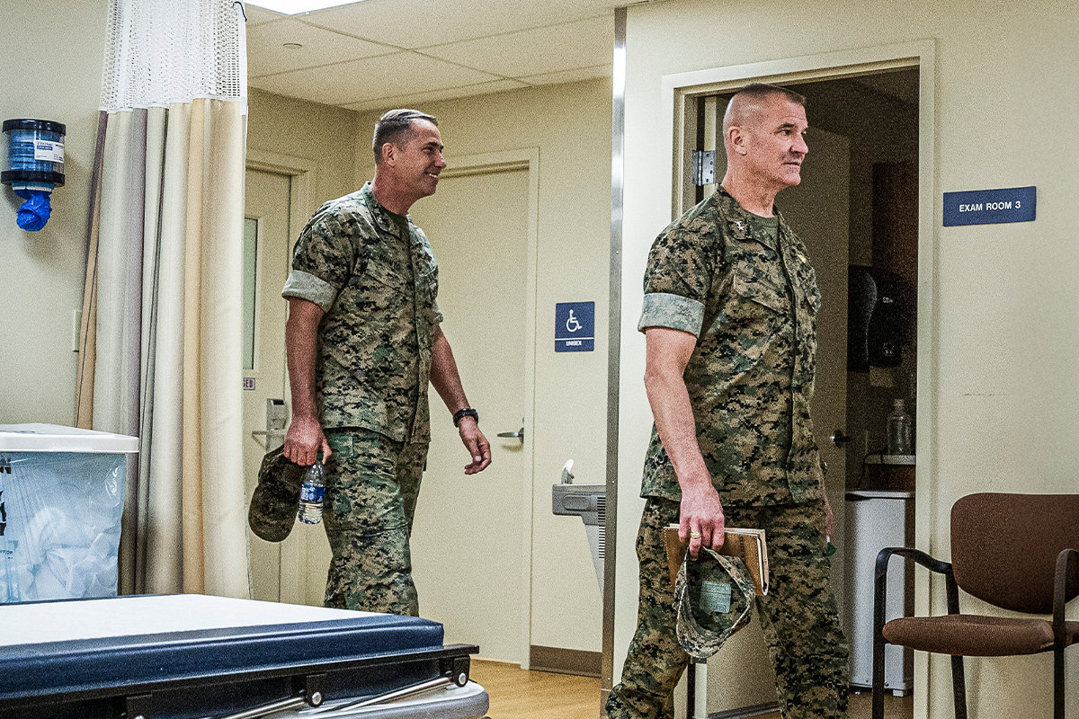 Marine personnel in camouflage walking through medical clinic examination room with health equipment.