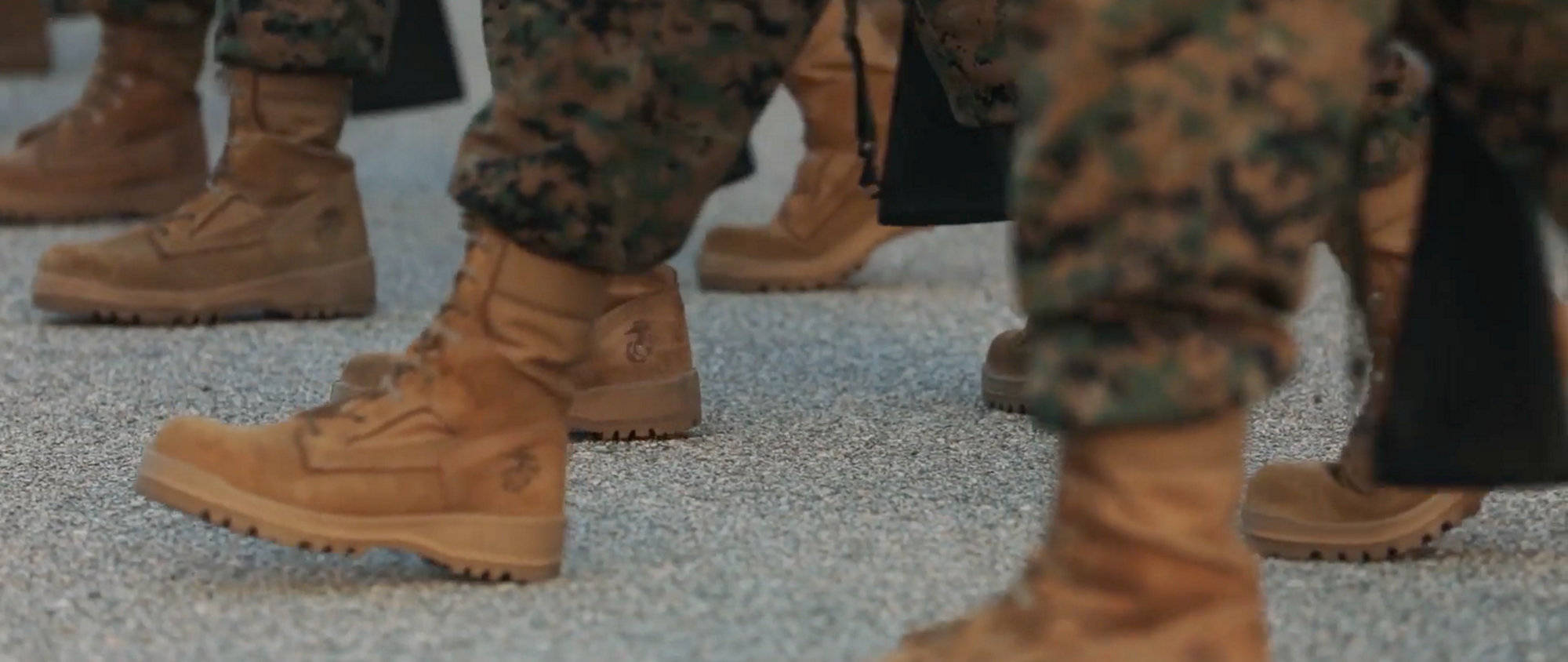 Marines in camouflage uniforms and boots, marching.