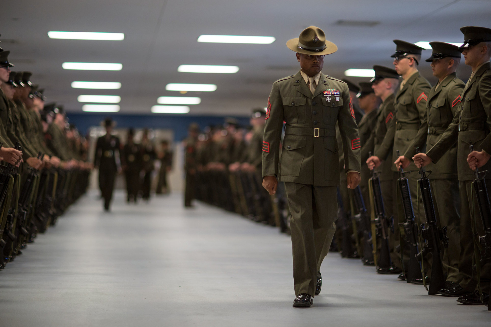 Marine drill instructor in campaign hat conducting formal inspection of recruits in formation.